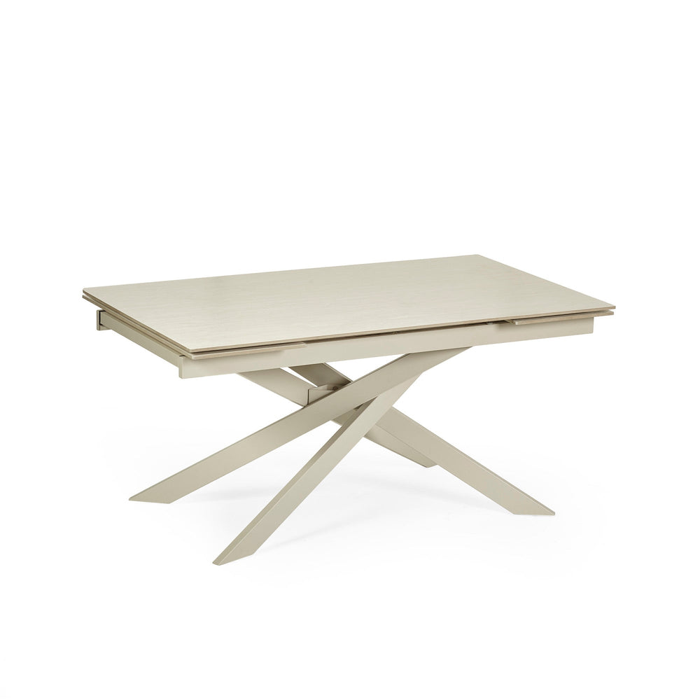 Top-down view of closed light beige extending dining table with cream crossed metal legs on white background