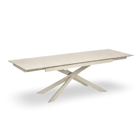 Light beige extending dining table fully extended with crossed cream metal legs on white background