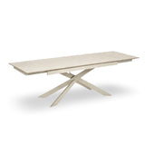 Light beige extending dining table fully extended with crossed cream metal legs on white background