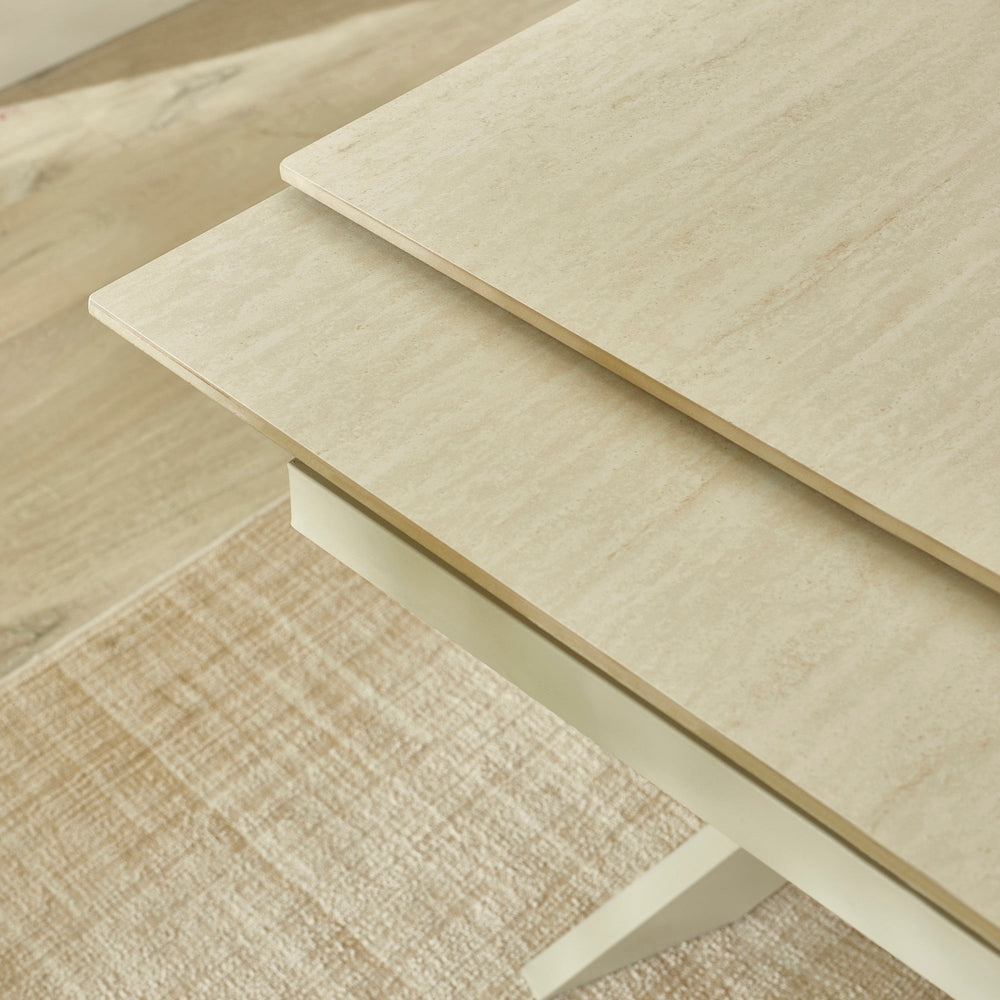 Close-up of cream crossed metal legs supporting light beige extending dining table on textured beige rug