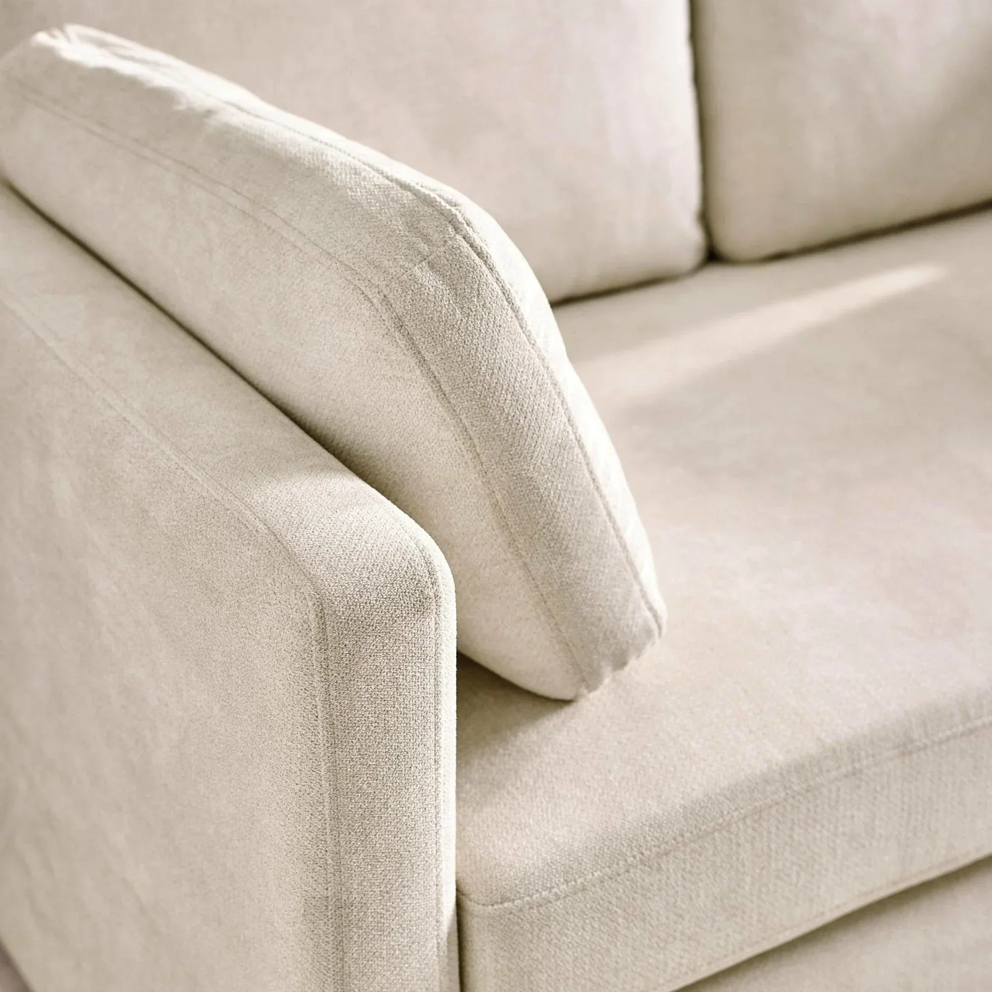 Beige fabric sofa armrest and cushion close up showing textured upholstery