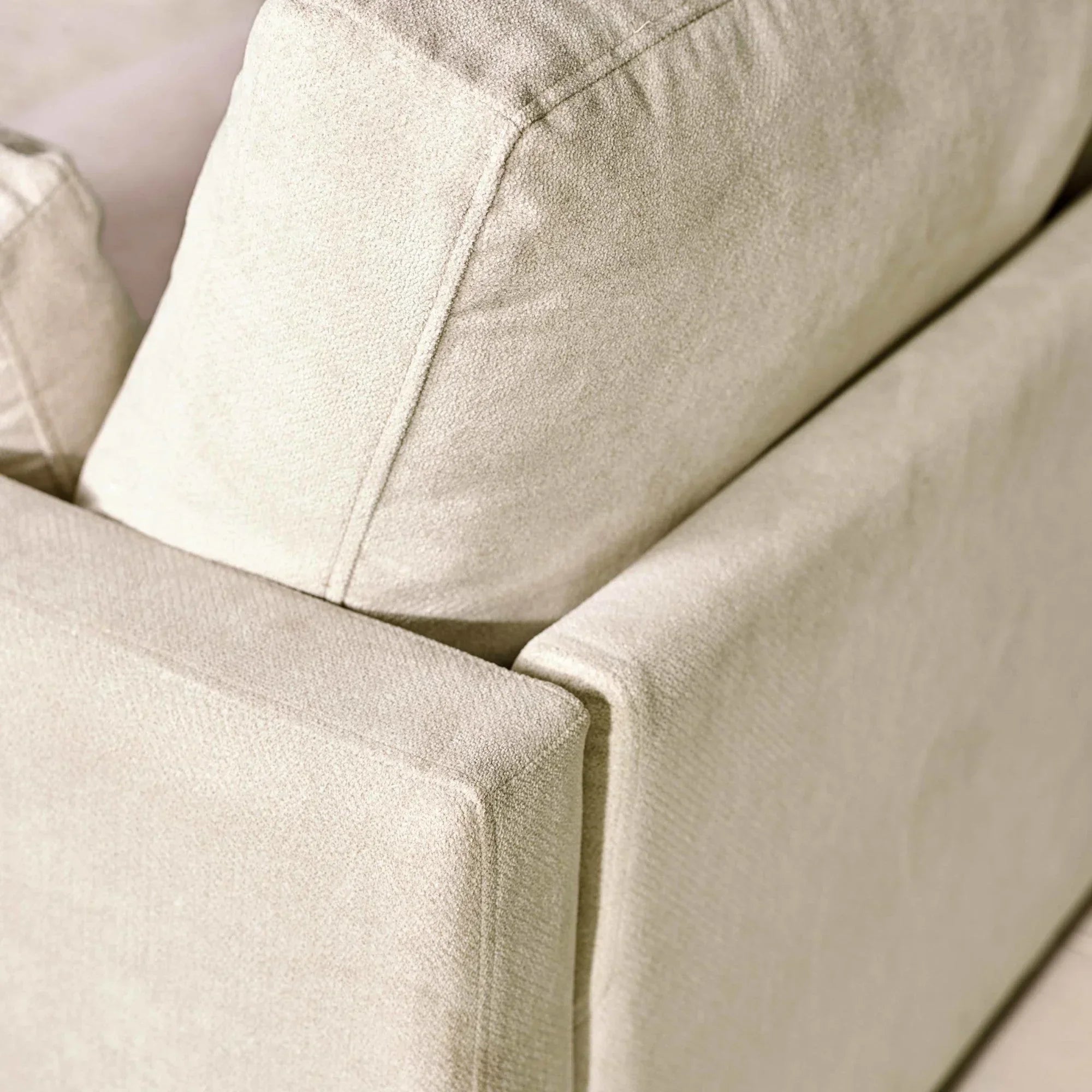 Closeup of beige fabric sofa corner with plush back and seat cushions