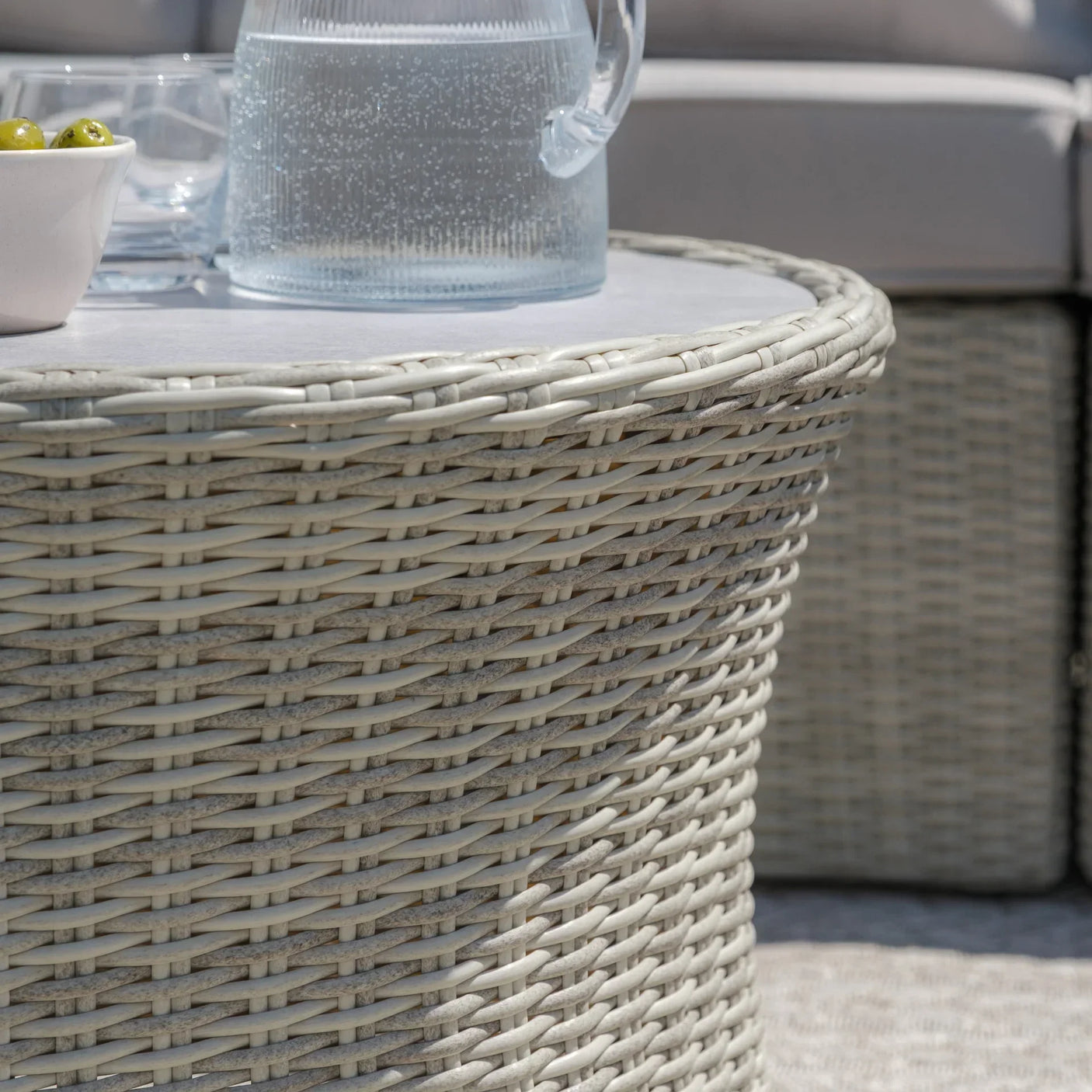 round rattan outdoor coffee table with glass jug and bowl, close-up of woven texture