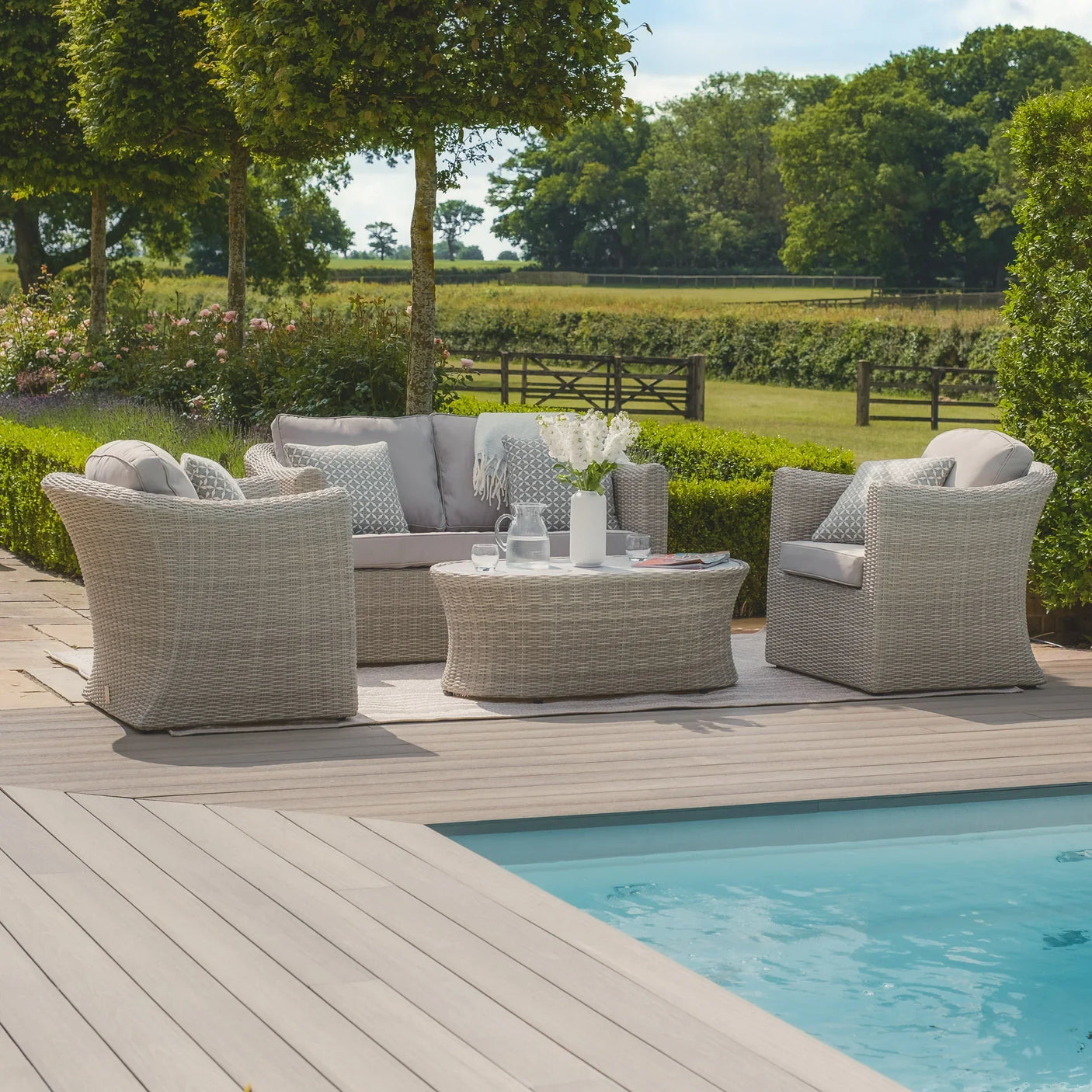 Grey rattan outdoor furniture set with cushions and coffee table beside a pool on patio