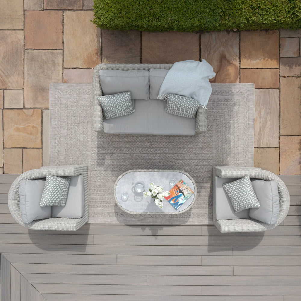 Grey rattan garden furniture set with sofa, two armchairs, and oval coffee table on patio