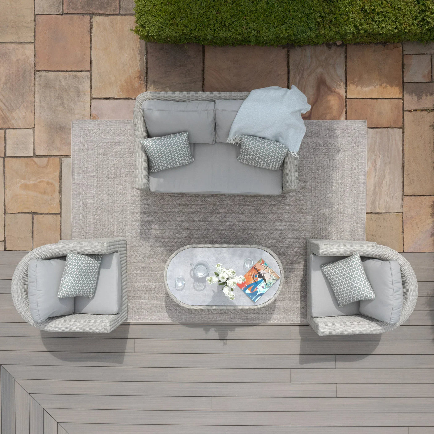 Grey rattan garden furniture set with sofa, two armchairs, and oval coffee table on patio