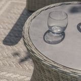 Round rattan outdoor coffee table with glass top and clear tumbler on patterned rug
