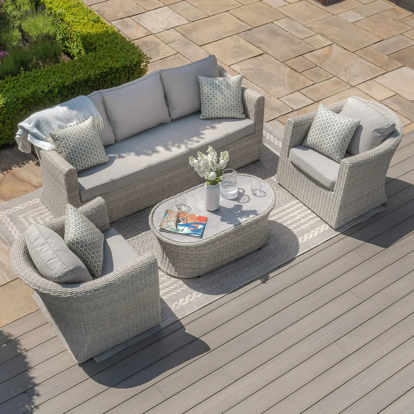 Rattan garden furniture set with grey cushions, armchairs, and coffee table on patio decking