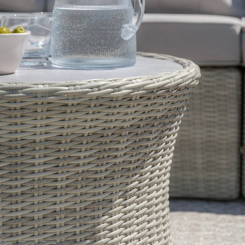 Round rattan garden coffee table with glass top, pitcher and bowl on patio