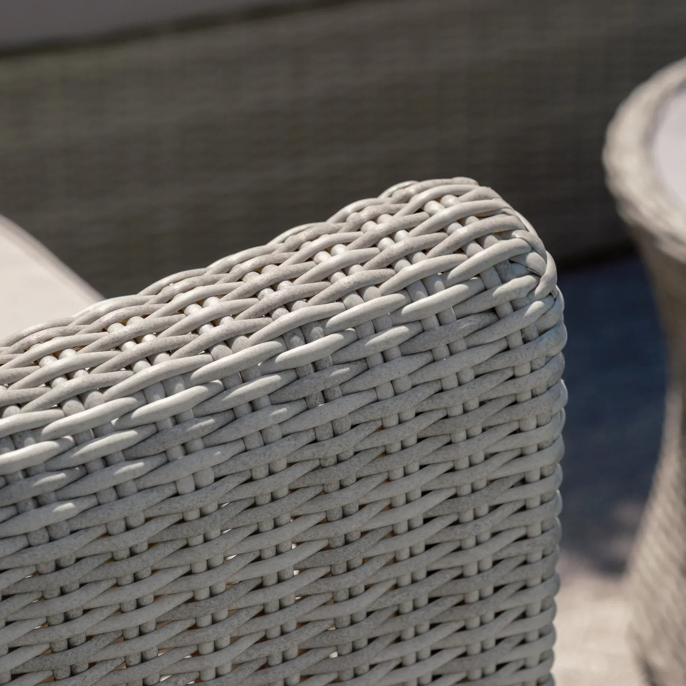 Light grey rattan garden sofa armrest with woven texture and outdoor setting