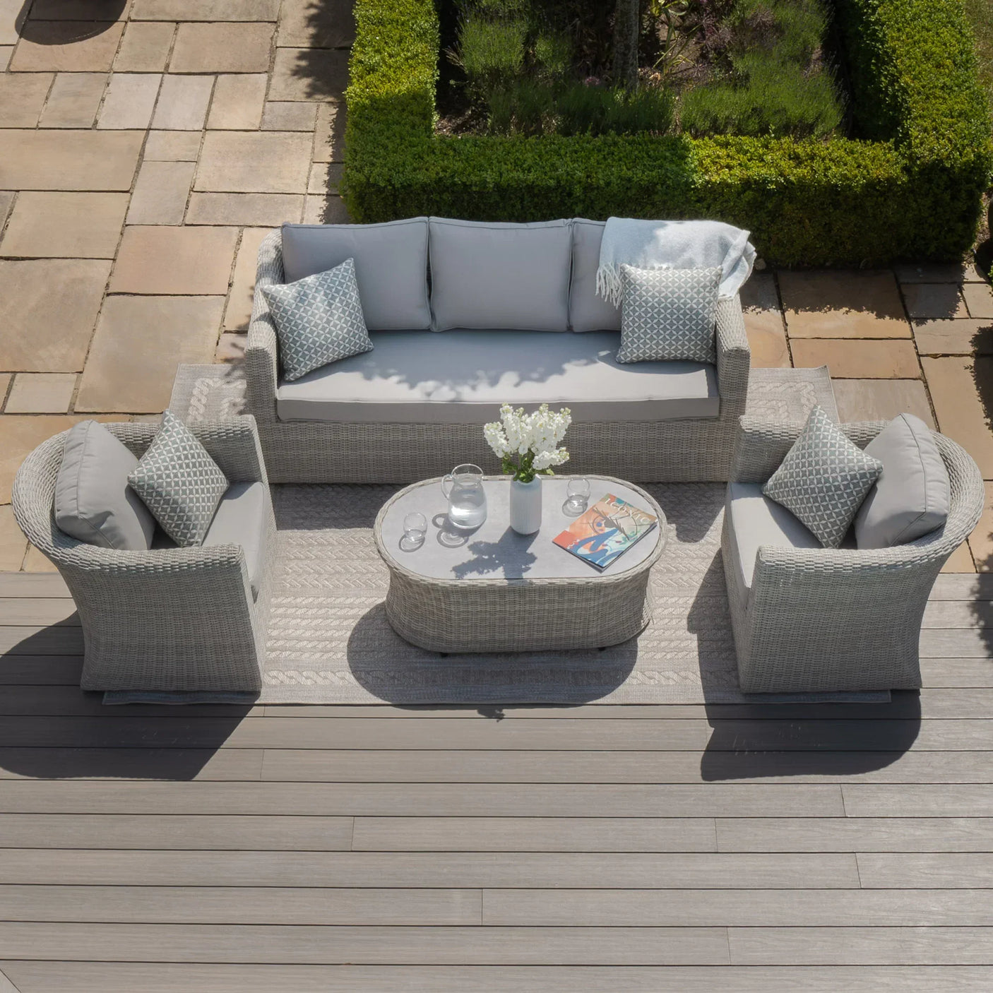 Light grey rattan garden sofa set with two armchairs and coffee table on patio decking