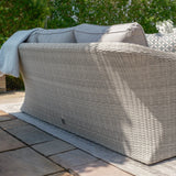 Light grey rattan outdoor sofa with cushions on stone patio facing garden greenery