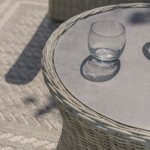Round rattan outdoor side table with glass top and clear tumbler on patterned rug