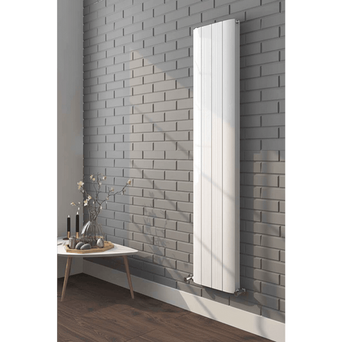 White vertical radiator on a gray brick wall with a small table and decorative items below.