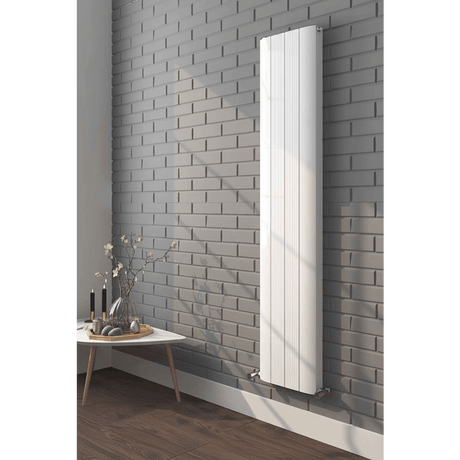 White vertical radiator on a gray brick wall with a small table and decorative items below.