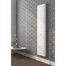 White vertical radiator on a gray brick wall with a small table and decorative items below.