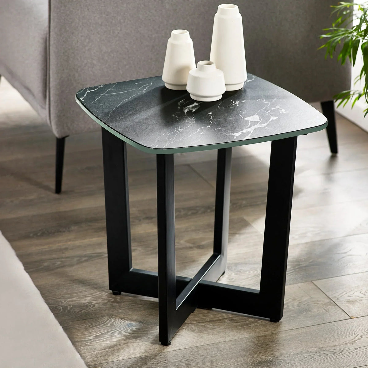 Black marble lamp table with modern metal legs beside grey sofa on wooden floor
