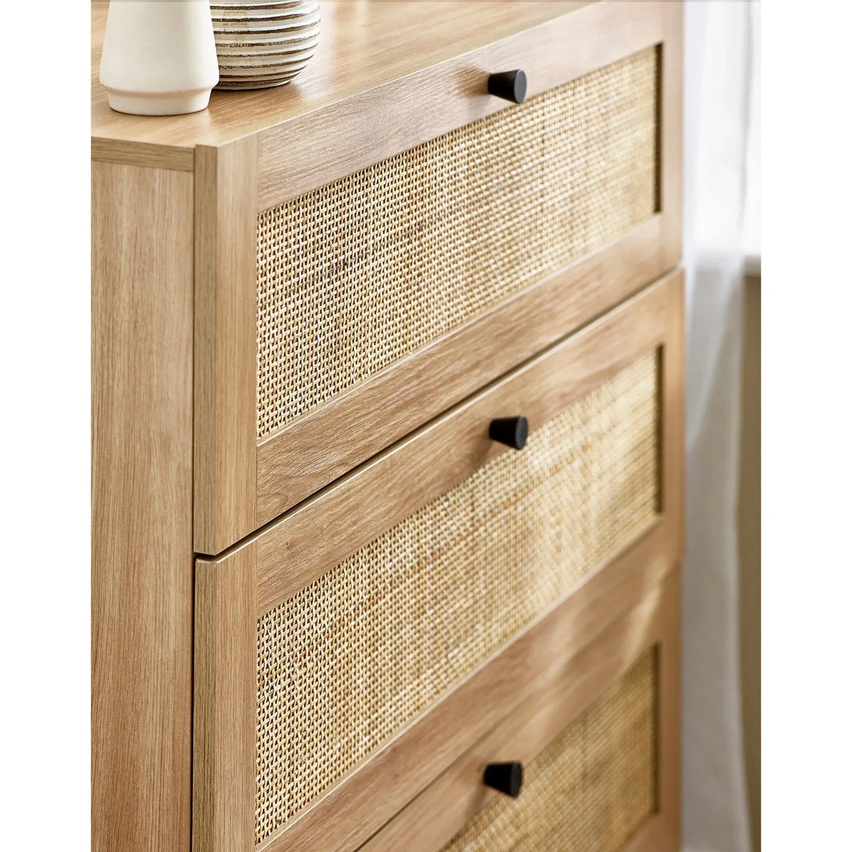 Oak three drawer chest with rattan fronts and black handles, close-up angle