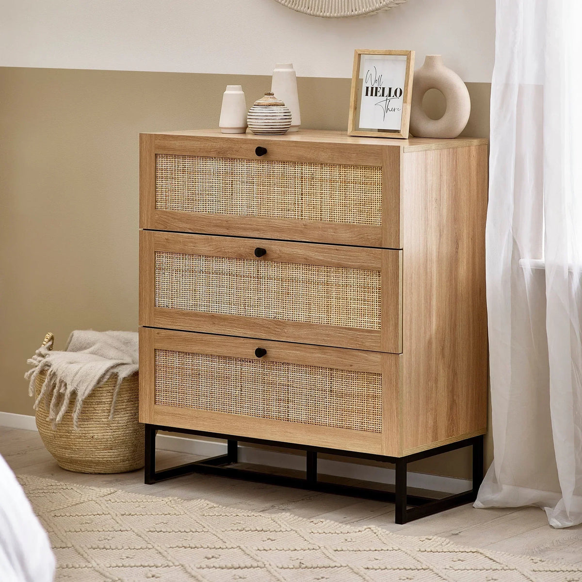 Oak three drawer chest with rattan fronts and black metal base in modern bedroom setting
