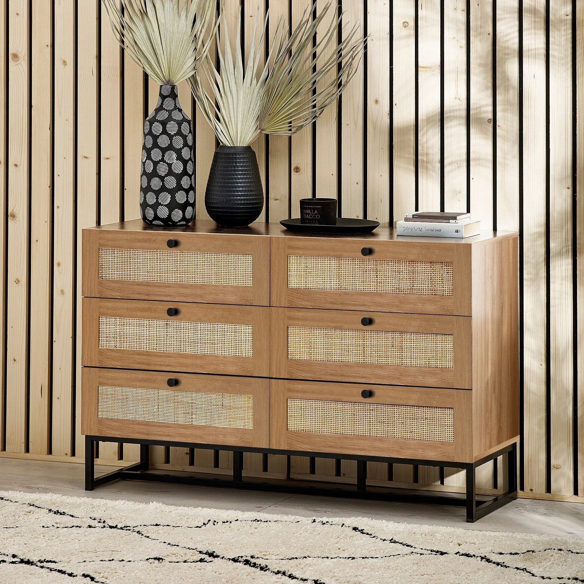 Oak 6 drawer chest with rattan fronts and black metal legs against wood panel wall