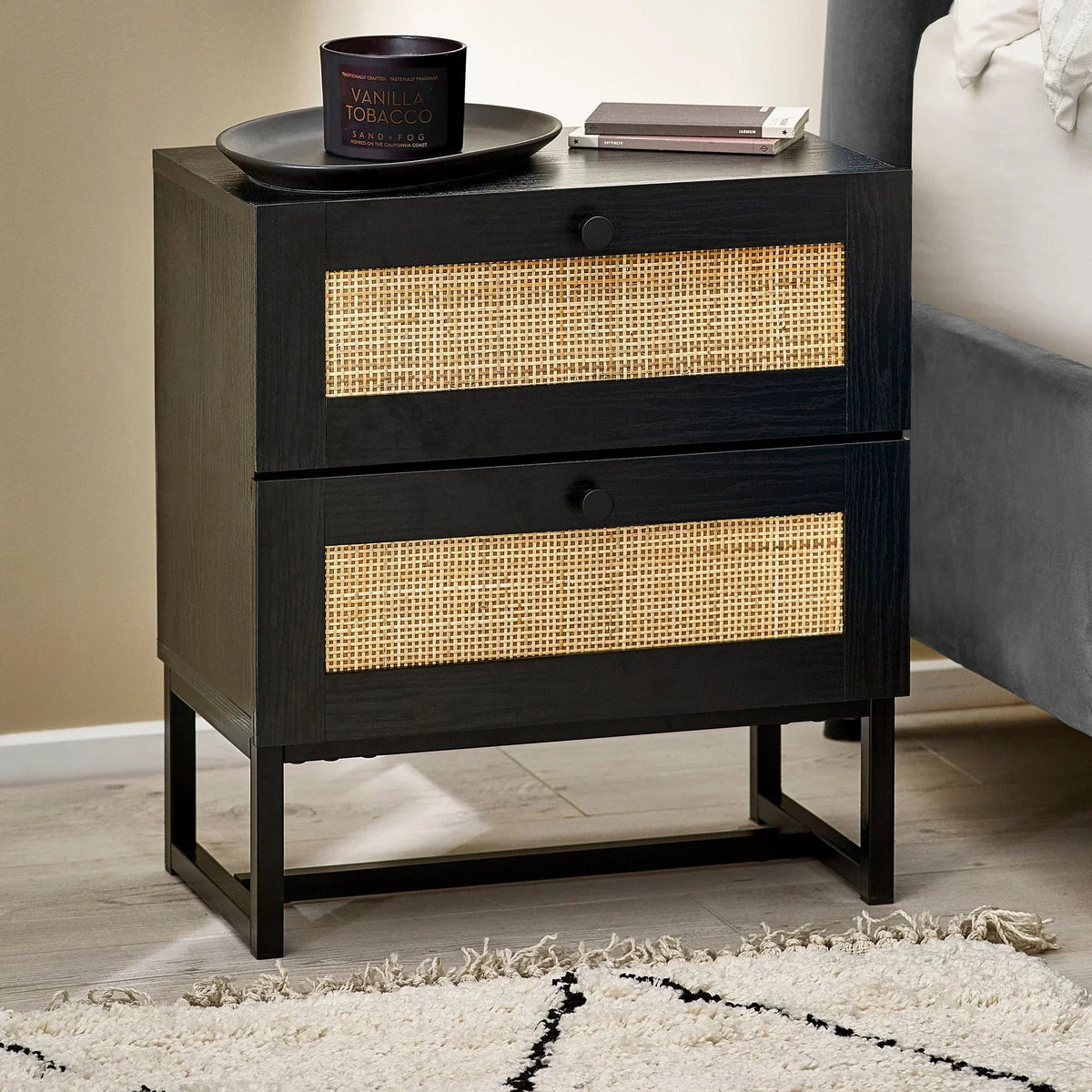 Black two-drawer bedside table with rattan fronts beside bed in modern bedroom setting