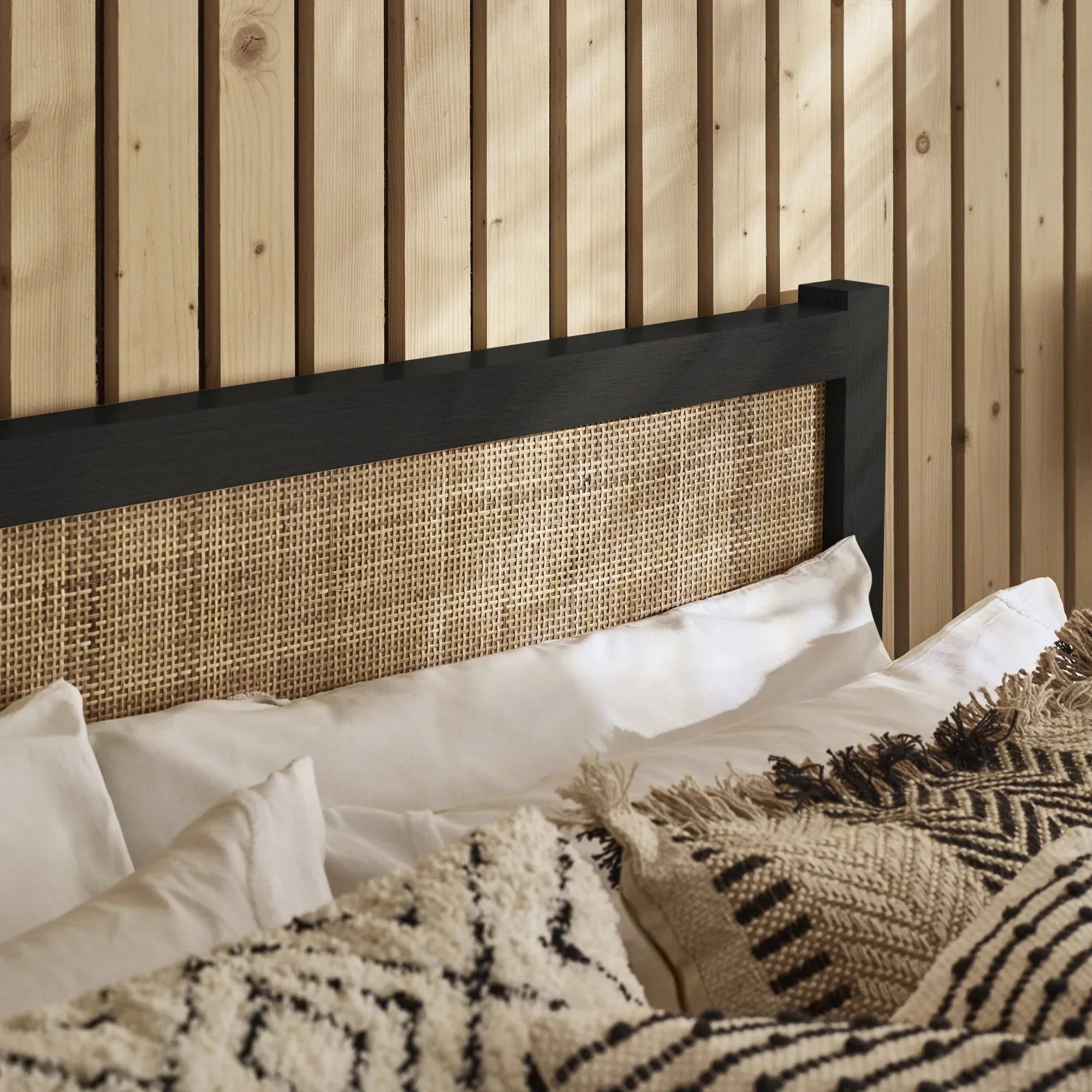 Black rattan double bed headboard with woven detail and patterned cushions