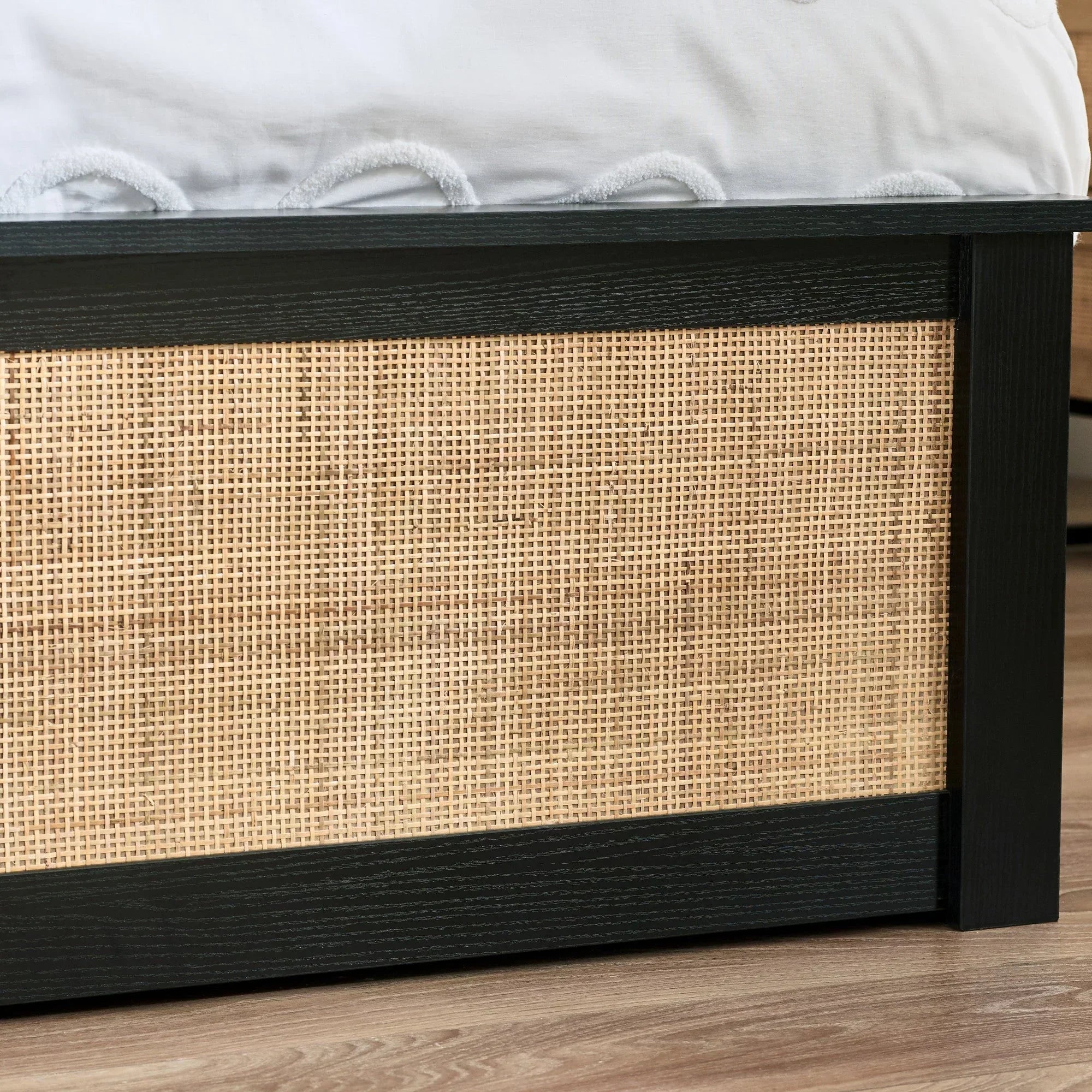 Black rattan ottoman with woven cane panel and wooden frame on hardwood floor