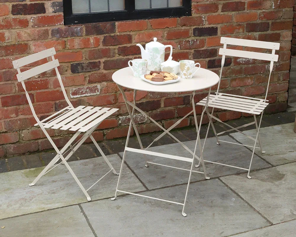 Champagne metal bistro set with round table, two folding chairs, and tea set on patio