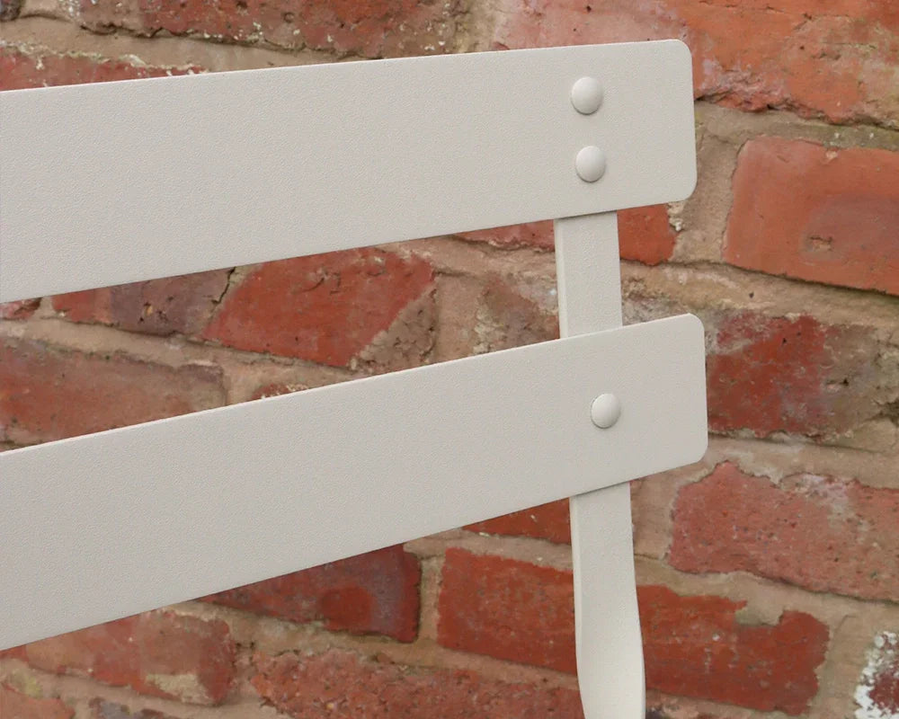 Champagne metal chair backrest with slats and rivets against brick wall