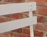 Champagne metal chair backrest with slats and rivets against brick wall