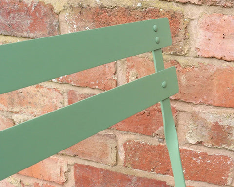 Olive green metal chair backrest detail against rustic brick wall