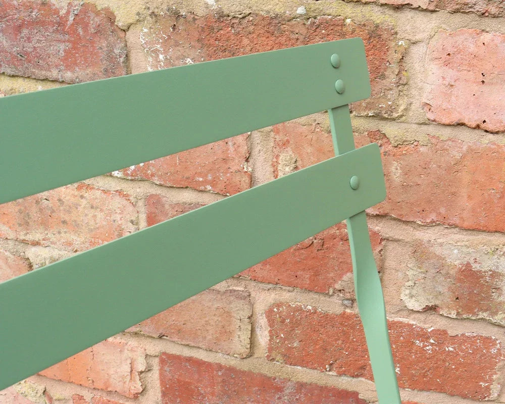 Olive green metal chair backrest detail against rustic brick wall