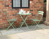 Olive green metal bistro set with round folding table and two chairs on patio by brick wall