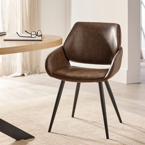 Brown upholstered dining chair with tapered black metal legs beside light wood round table in neutral room.