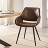 Brown upholstered dining chair with tapered black metal legs beside light wood round table in neutral room.