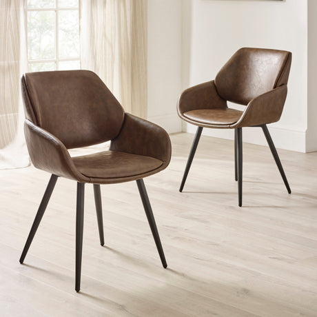 Two brown upholstered dining chairs with black tapered legs on light wood floor near large window.