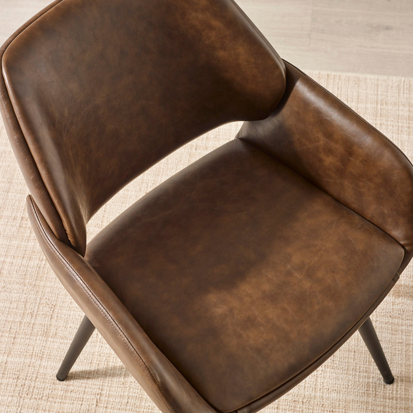 Close-up of brown upholstered dining chair seat and armrests, black metal legs visible on beige carpet.