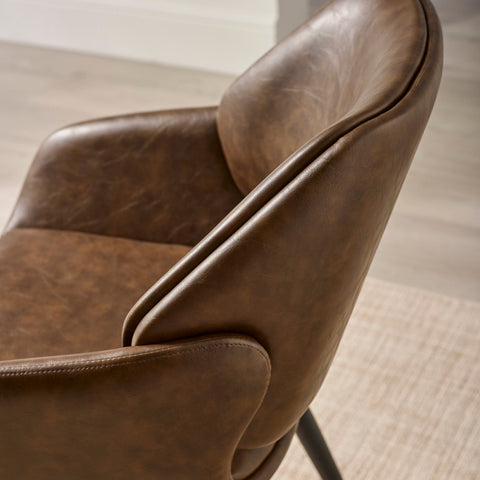 Close-up of brown upholstered dining chair backrest and armrest showing texture and stitching details.