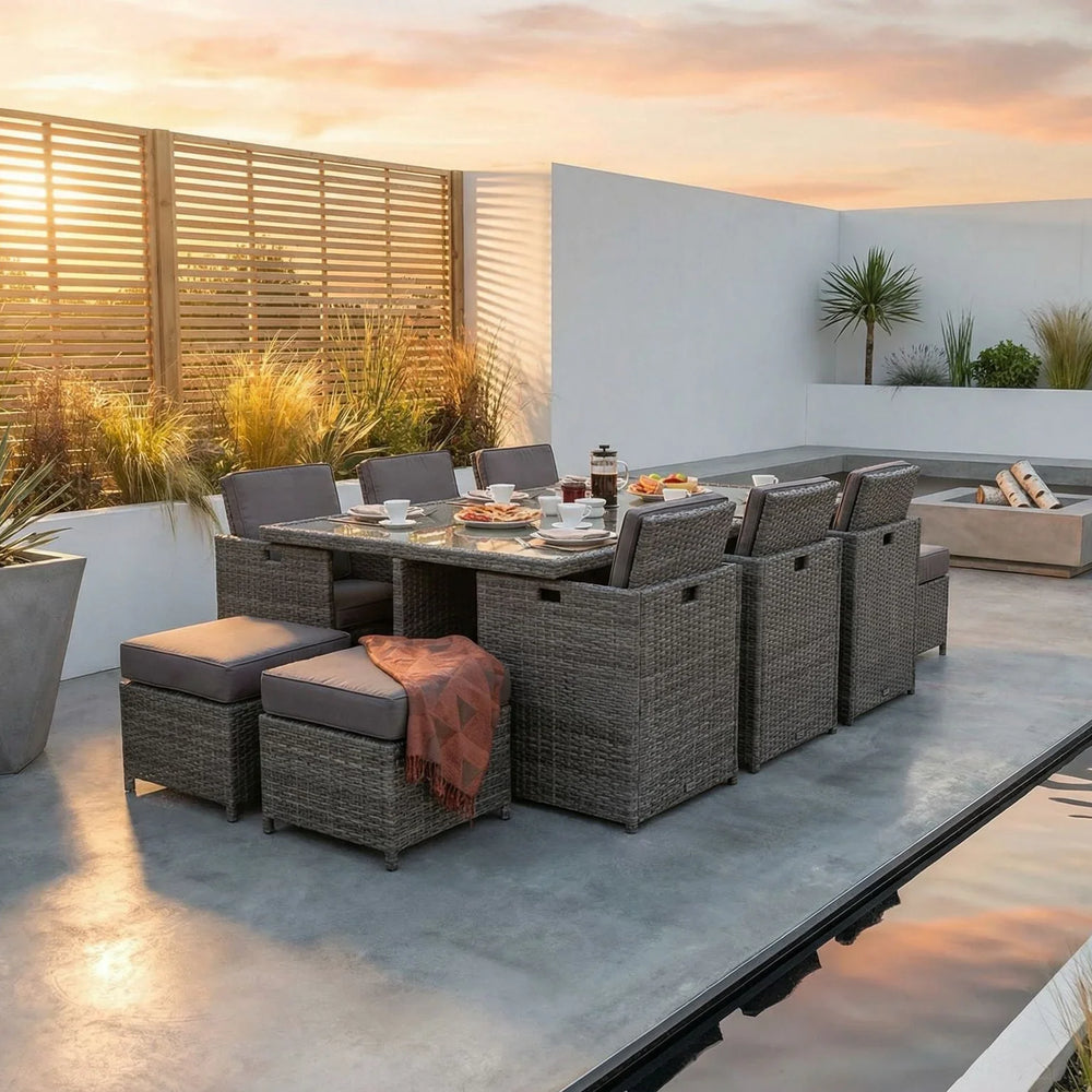Rattan outdoor dining set with grey cushions and glass table on modern patio at sunset