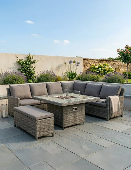 Grey rattan corner garden sofa set with glass fire pit table and bench on stone patio