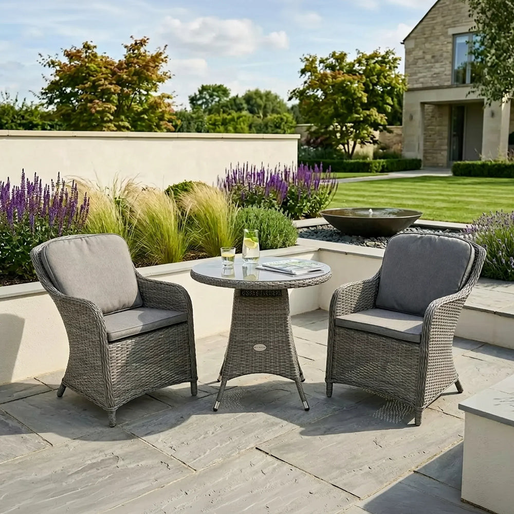 Grey rattan garden furniture set with round table and two armchairs on stone patio