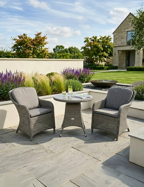 Grey rattan garden bistro set with round table and two cushioned chairs on patio