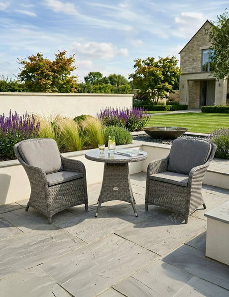 Grey rattan garden bistro set with round table and two cushioned chairs on patio