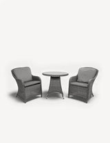 Grey rattan bistro set with two cushioned armchairs and round table on white background