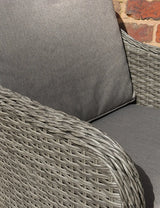 Close up of grey rattan garden chair with woven armrest and padded seat cushion