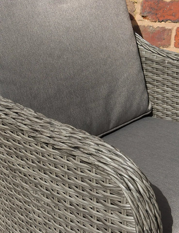 Close-up of grey rattan garden chair with thick grey cushions and woven arm detail