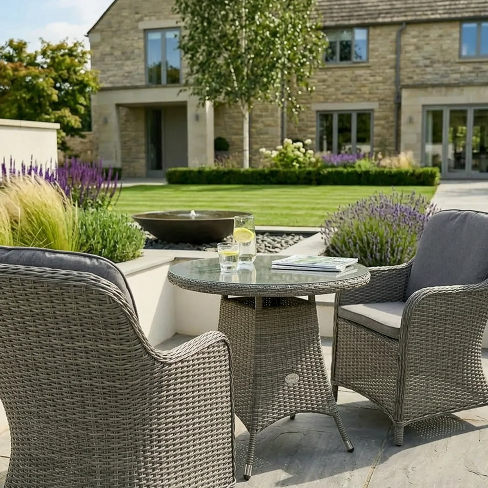 Grey rattan garden bistro set with two armchairs and glass top table on a patio