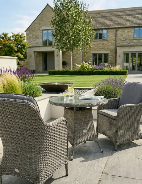 Grey rattan garden bistro set with two armchairs and glass top table on a patio