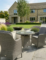 Grey rattan garden furniture set with glass top table and cushioned chairs on stone patio