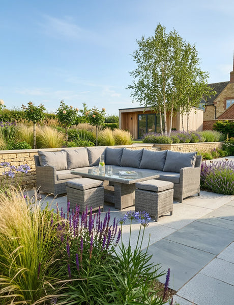 Grey rattan corner garden sofa set with glass table and stools on stone patio